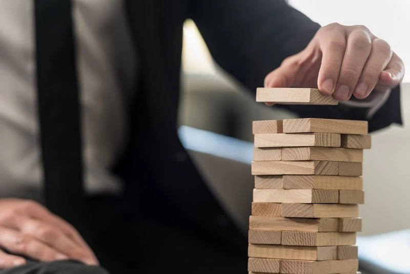 Close-up of a professional building a wooden block tower, symbolizing sustainable growth and compliance strategy for VCFMs.