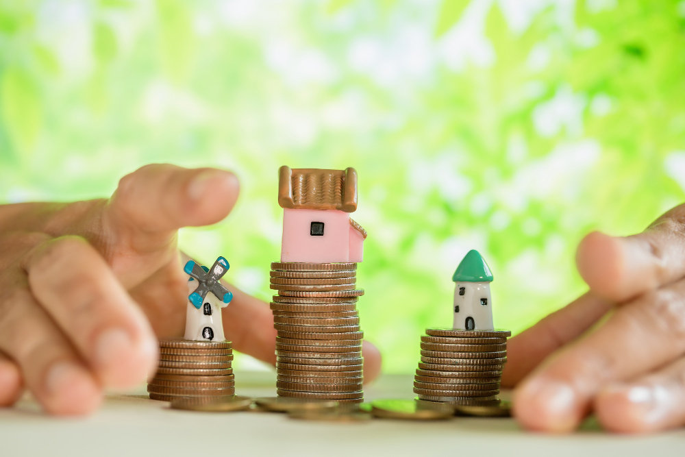 A person holds a stack of coins with a small house placed on top, symbolizing financial investment in real estate.