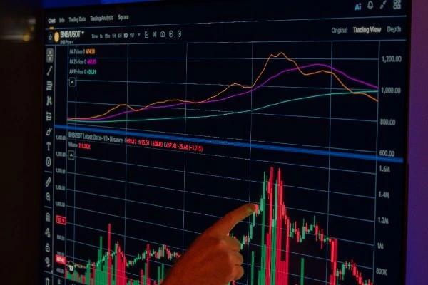 A hand points to a dynamic cryptocurrency market chart displayed on a screen.