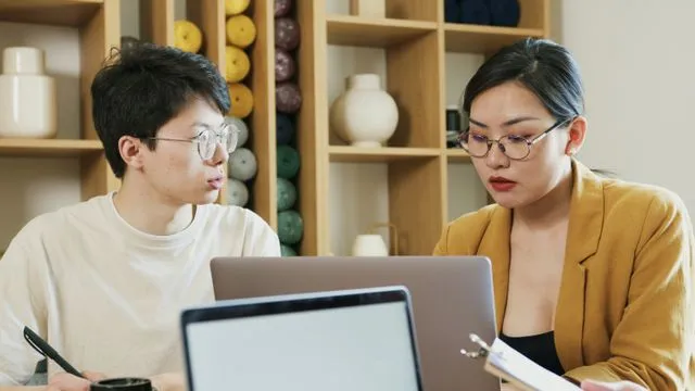 Two professionals working together in a modern office setting using laptops.