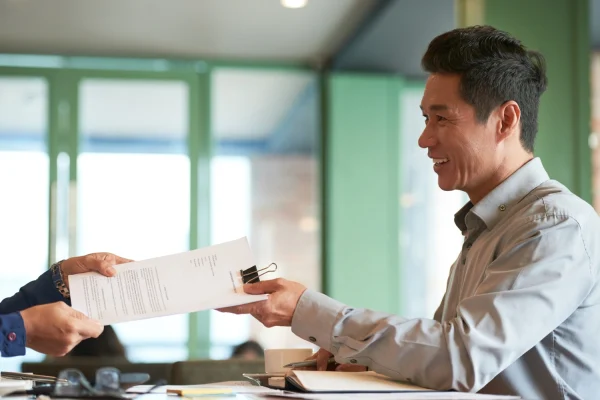 Business consultant handing regulatory documents to a client during a corporate advisory meeting. 