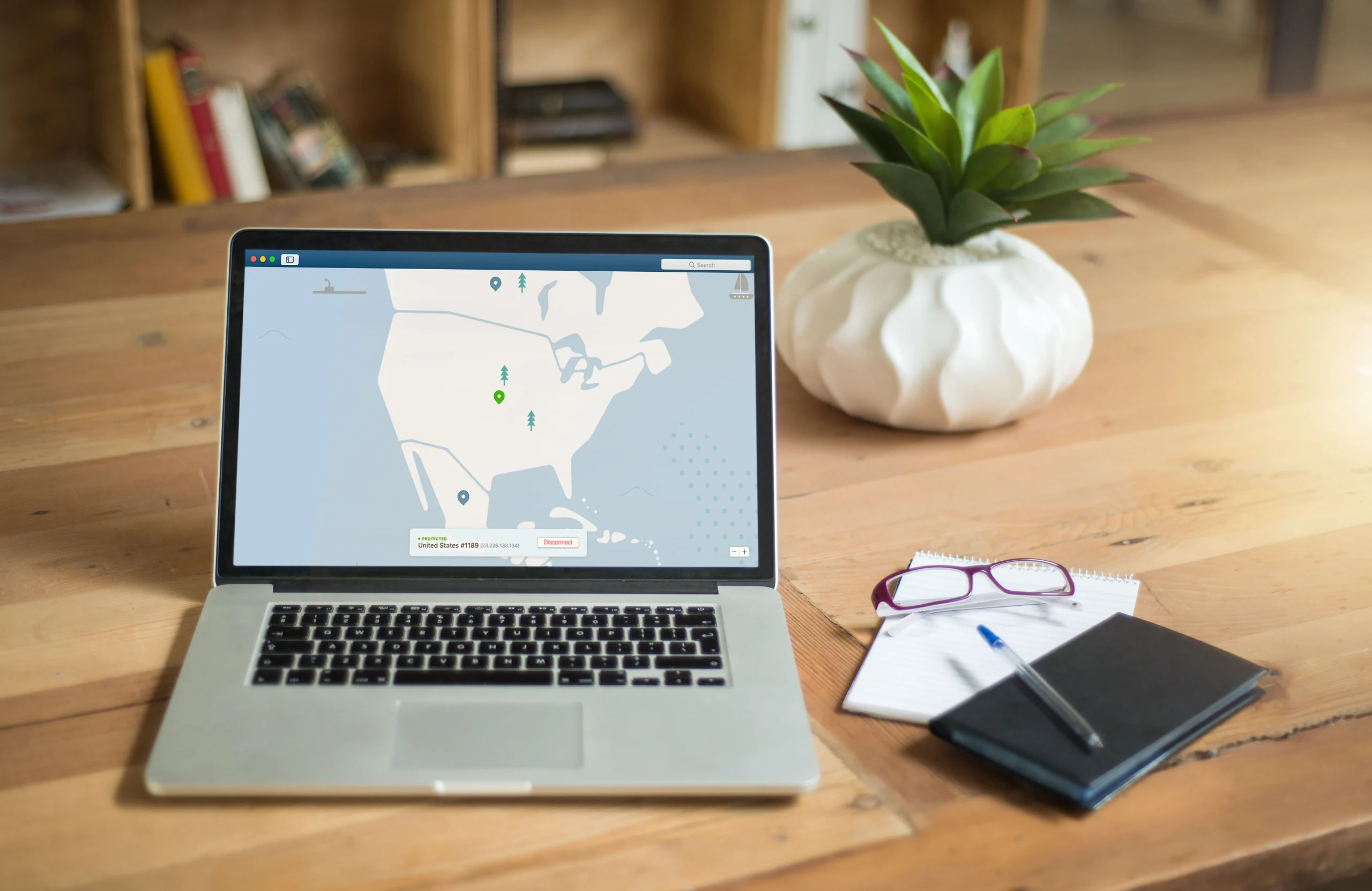 A laptop displaying VPN software sits on a wooden desk with a notepad and plant offering a secure workspace vibe