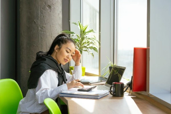 Financial compliance consultant working at a desk with a calculator and laptop, reviewing MAS licence variation documents.